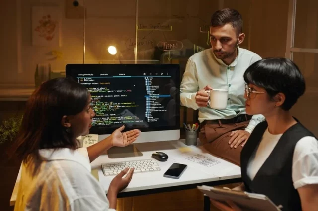 Team discussing code around a computer in an office setting.